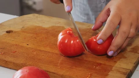 A woman's hands slice red tomatoes on a table with vegetables. Medium shot. Stock Footage 340472740