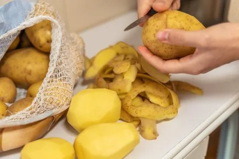 Womans hands with small kitchen knife. Bag with unpeeled potatoes. Foto stock