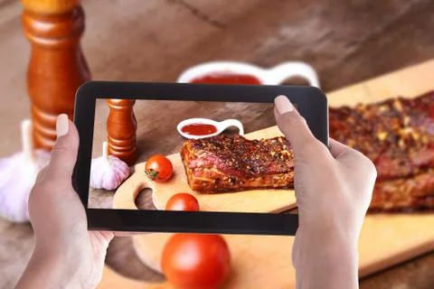 Woman's hands with a smartphone on the screen of which photo Grilled pork ribs Stock Photos
