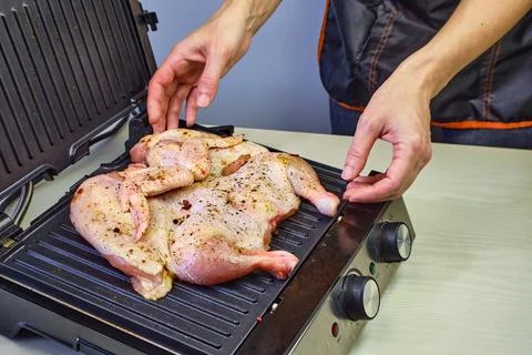 The woman's hands spread the raw chicken in seasonings on an electric grill. Raw Stock Photos