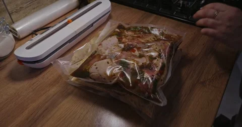 Womans hands stacking vacuum-sealed bags of raw marinated chicken meat on a Stock Footage 329860088