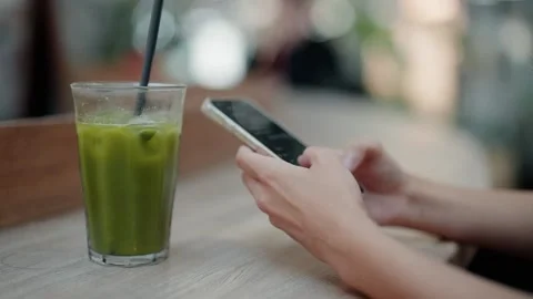 Woman's hands texting on smartphone at cafe table with matcha latte Stock Footage 343909981