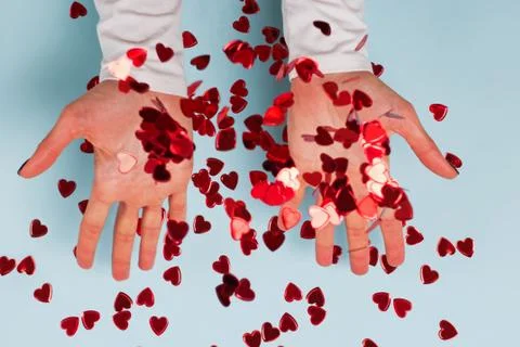 Woman's hands throwing up red heart shaped glitter confetti on blue background Stock Photos