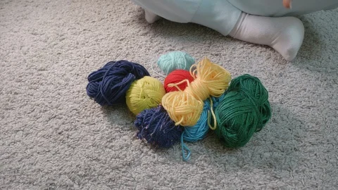 Woman's hands touch several colourful balls and skeins lying on the floor. My Stock-Footage 129140286