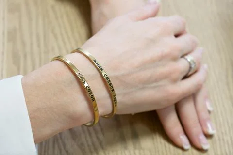Womans hands with two thin gold bracelets. Simple jewelry with printed insc.. Stock Photos