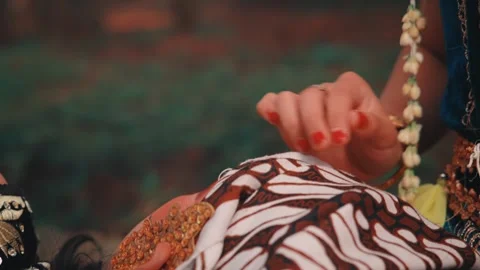 A Woman's Hands Tying a Batik Headwrap on Her Partner Stock Footage 313473006