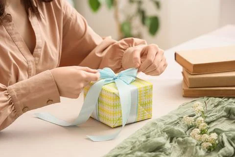 Womans hands tying light blue ribbon bow on yellow patterned gift box for cel Stock Photos