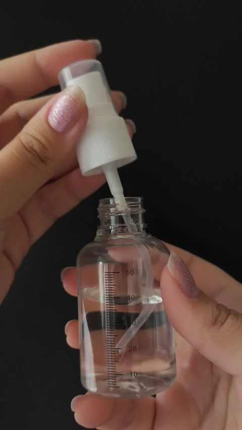 A womans hands unscrew or twist the spray bottle cap on a black background Stock Footage 314975375