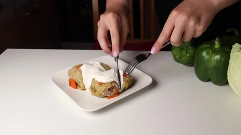 A woman's hands use a knife and fork to cut off a piece of cabbage roll to try Stock Footage 280649824