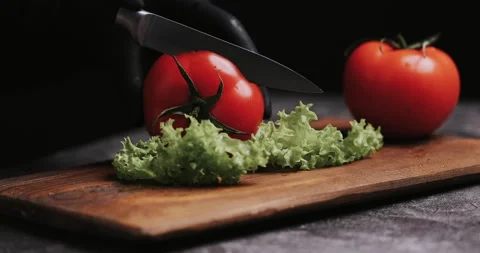 Woman's hands using kitchen knife cutting fresh tomato on wooden cutting board.  Video stock 148245230