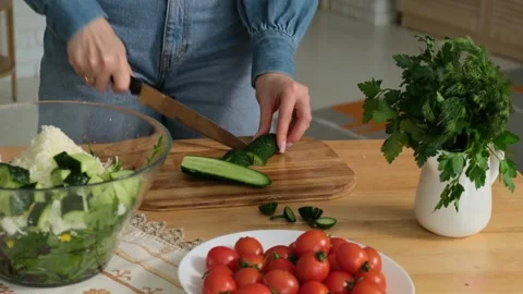 Woman's hands using a kitchen knife to slice fresh cucumber on a wooden board Stock-Footage 345048260