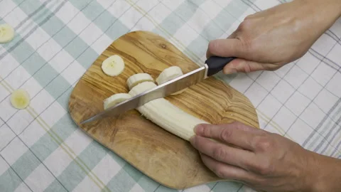 Woman's hands using knife to cut banana into slices on cutting board - high shot Stock Footage 341227052