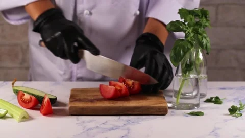Woman's hands in white apron black gloves cutting tomato on green board, behind Stock Footage 167154384