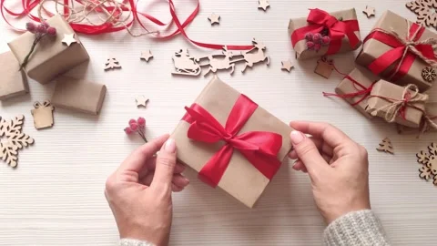 Woman's hands wrap christmas present in craft paper with red ribbon and berries. Stock Footage 165394481