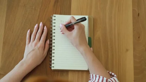 Woman's hands writing a to-do list in a notebook on a wooden table, diligently p Stock Footage 335241771