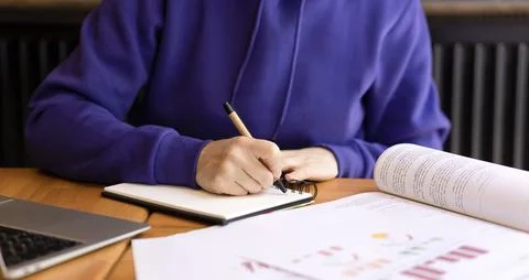 Woman's hands writing notes with pen in notebook, books and textbooks on table. Stock Photos
