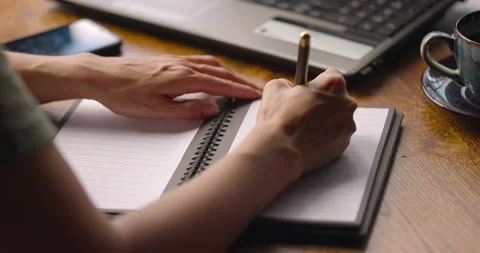 Woman's hands writing on paper notebook page sitting with a cup of coffee and Stock Footage 159770230