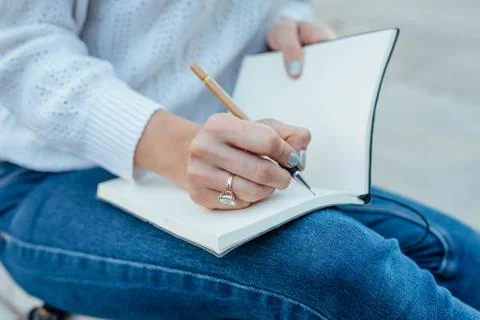 Woman's hands is writing something at the notebook. Outdoor background. Stock Photos