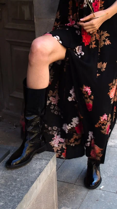 A woman's leg in a leather boot and black floral dress developing from the wind Stock Footage 248528691