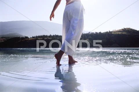 Woman's legs outdoors walking on water in scenic location (lens flare) Stock Photos