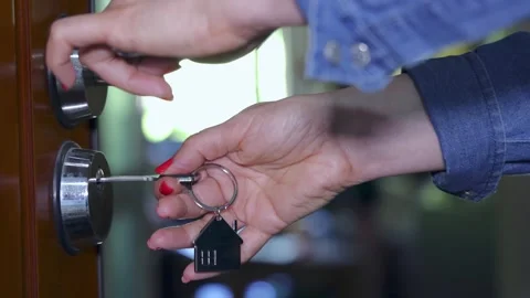 Woman's locks or unlocks the apartment door with a key and small house keychain Stock Footage 308025543