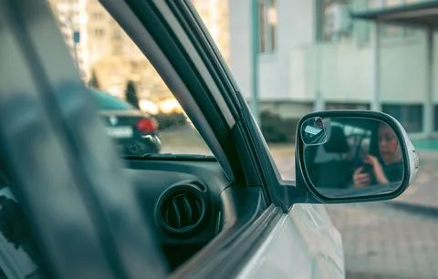 Womans reflection in car side mirror, soft city light, smartphone in hand, c Stock Photos