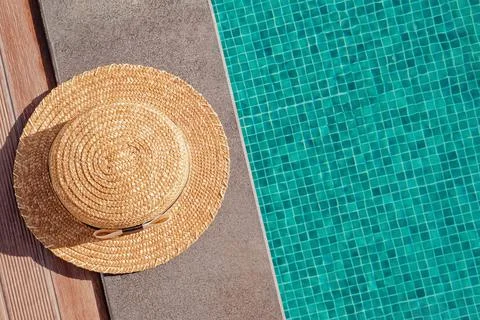 Woman's straw hat lying on the edge of the swimming pool with turquoise water Stock Photos