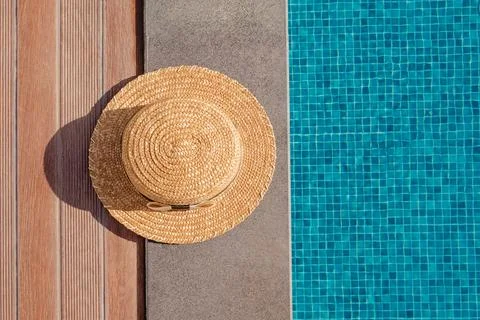 Woman's straw hat lying on the edge of the swimming pool with blue water Stock Photos