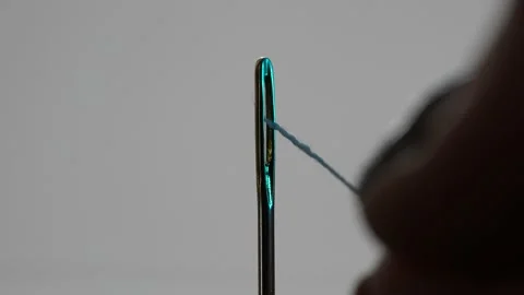 A woman's tailor hand insert With sewing thread in a needle hole. fabric clot Stock Footage 176364556