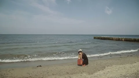 A womanSitting and looking pebbles on the beach Seagulls flying and swimming on Stock Footage 74397053