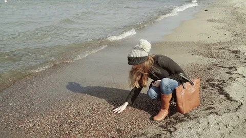 A womanSitting and looking pebbles on the beach Seagulls flying and swimming on Stock Footage 74397950