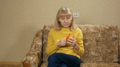 Women age eats fruit at home on the couch. She cuts off a piece of persimmon and Stock Footage 71243031