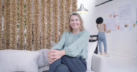 Women colleagues using tablet on sofa in studio, one calling arranging wall Stock Footage 340614026