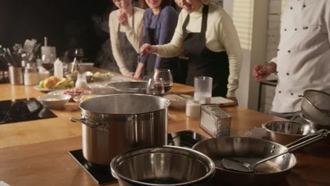 Women Cooking While Chef Teaching and Helping Them During Cooking Master Class Stock Footage 332574192