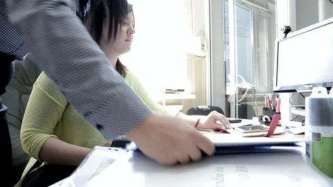 Women at the desktop in front of the computer turn the pages of the folder Stock Footage 114317519