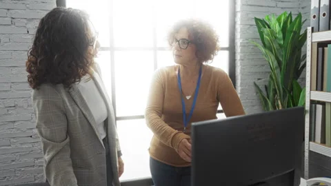 Women discussing work in an office with a computer and bookshelves, under b.. Stock Footage 303025473