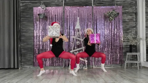 Women doing squats with gift boxes in hands. Fitness females in christmas hats Video stock 222573679