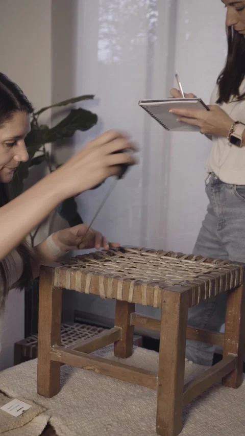 Women examining woven stool texture with focused attention Stock Footage 345758048