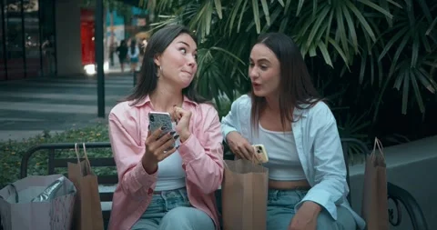 Women friends sitting bench using phones embodying positive communication Stock Footage 274518443