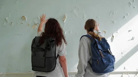 Women gesture at deteriorating plaster wall in abandoned space Stock Footage 342087815
