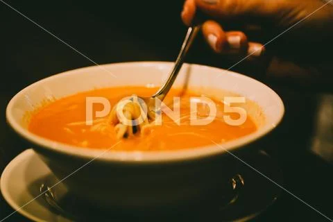Women hand takes spoon of tomato soup with pasta. Photography with vintage fi Stock Photos
