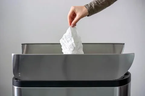 Women hand throwing a white used crumpled tissue paper into a trash bin. Stock Photos