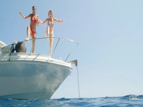 Women jumping off boat into ocean two girls jump into clear blue water from Stock Footage