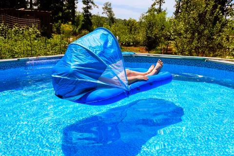Women rests on float in pool during sunny day surrounded by trees greenery 스톡 사진