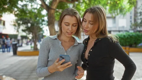 Women smiling while taking a selfie in a bustling urban park, showcasing fa.. Vidéo 305544084