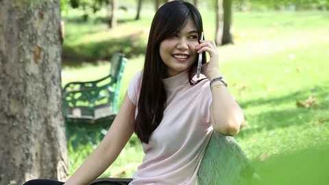 Women talking on smartphone while sitting on wood bench Stock Footage 75672460