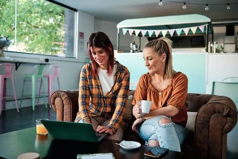 Women using a laptop while sitting on a sofa in a coffee shop. Stock Photos