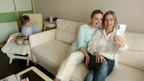 Womens are sitting on couch taking selfie, in background child is playing phone Video stock 153524103