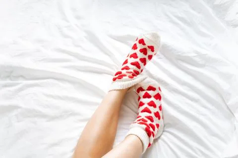 Women's feet in warm socks with red hearts on a white bed Stock Photos