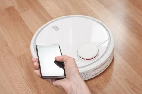 Womens hand using mobile to control white robotic vacuum cleaner. modern smar Stock Photos